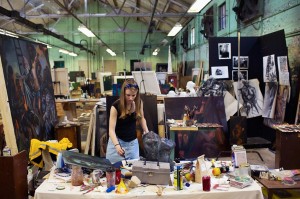 年轻的妇女工作在桌子上覆盖的艺术用品，在大仓库设置